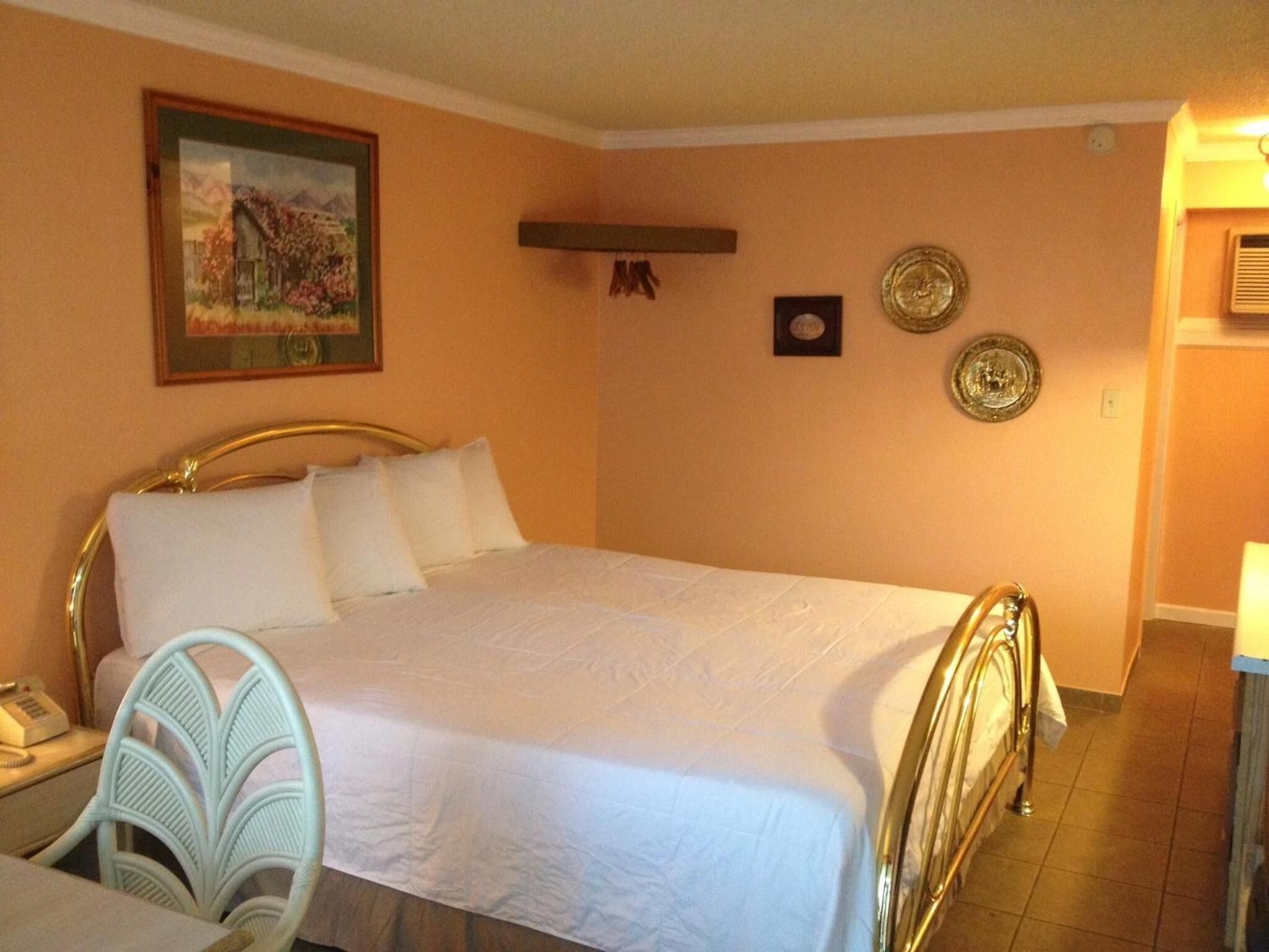 A bedroom with a bed, a chair, a desk, and a painting on the wall.