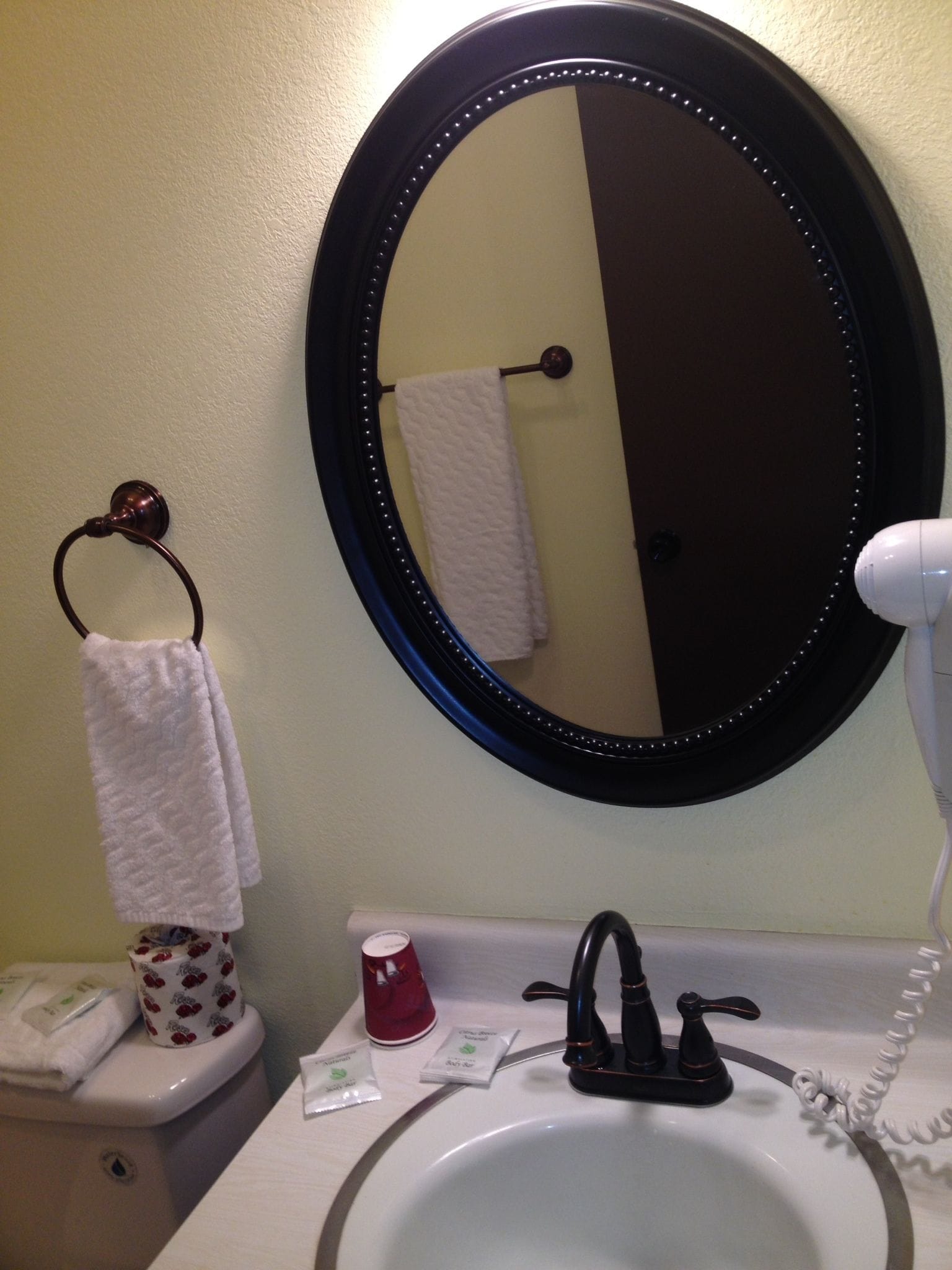 A bathroom with a round mirror, a sink, a towel rack, and toiletries.