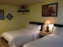 Habitación de hotel con dos camas, una mesita de noche con lámpara y una estantería de pared con flores.