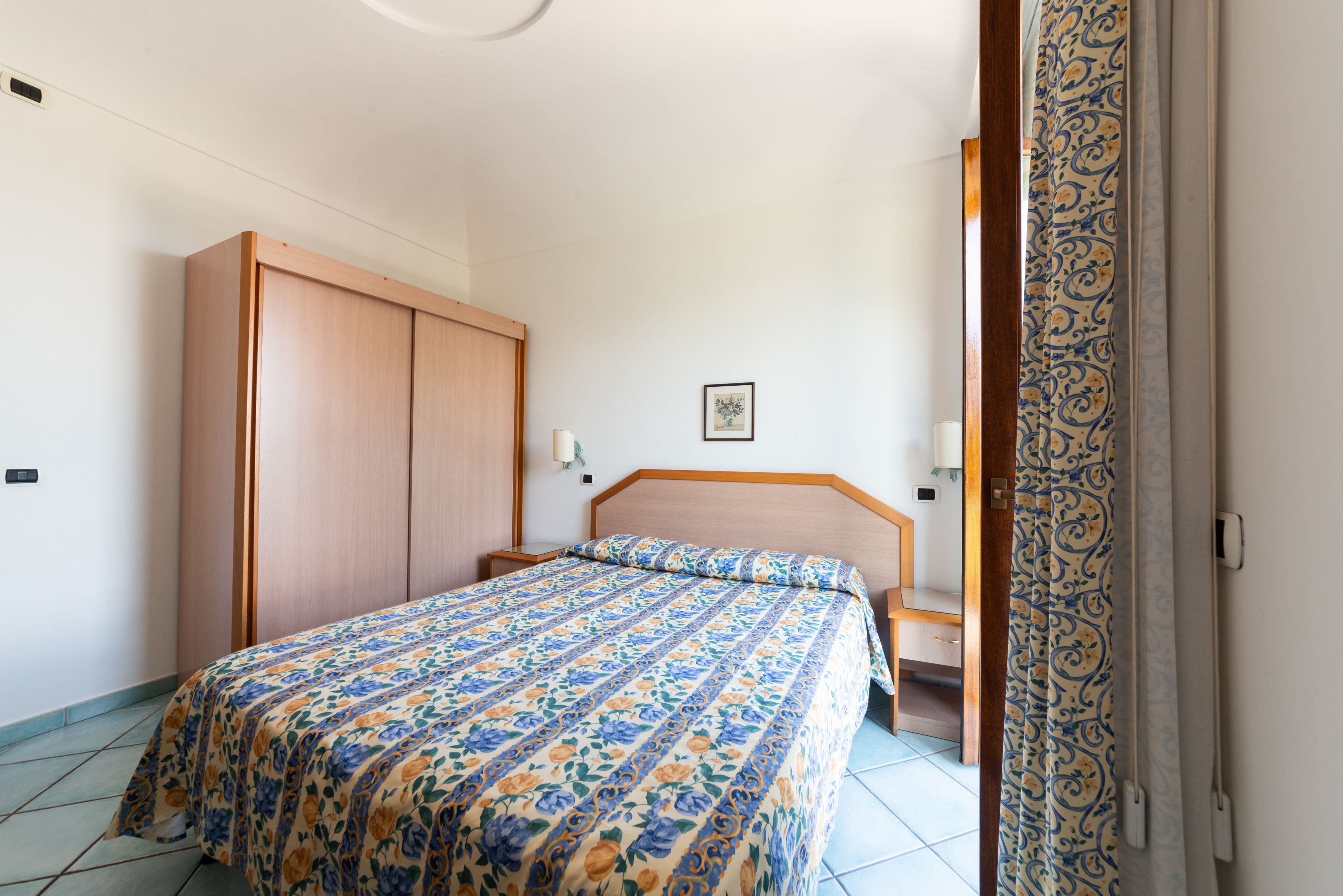 Un dormitorio con cama, armario de madera, mesita de noche y un cuadro enmarcado en la pared.