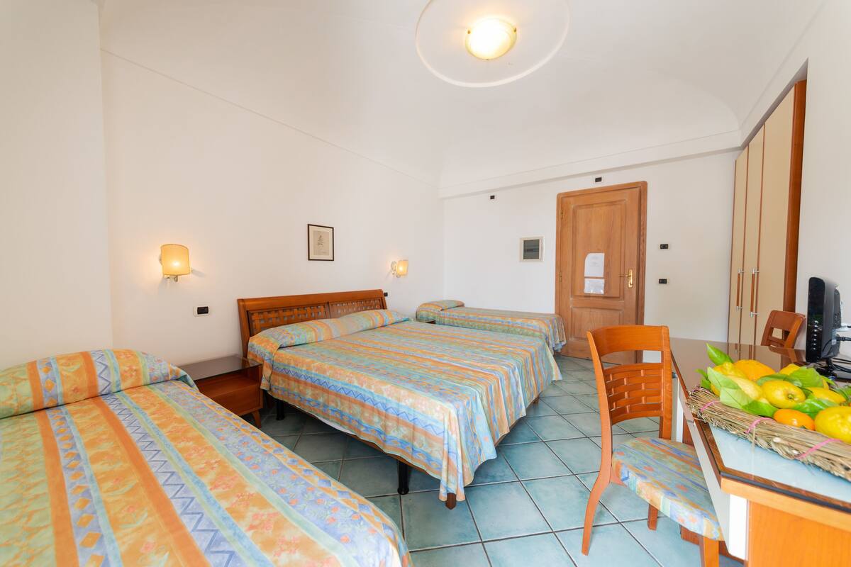 A room with three beds, a wooden desk, and a chair.