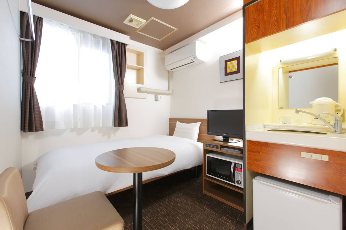 Une chambre d’hôtel avec un lit, une petite table, une télévision, un four à micro-ondes et un lavabo avec un miroir.