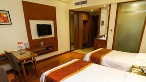 Une chambre d’hôtel avec deux lits, un bureau avec une chaise, une télévision et une salle de bain visible à travers une porte ouverte.