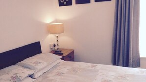 A neatly made bed with floral bedding, a bedside lamp, and three wall art pieces above it.