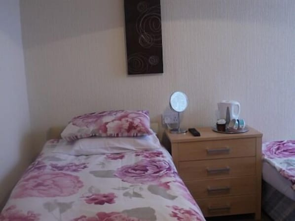 Una habitación de hotel con cama, mesita de noche, espejo y cafetera.
