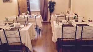 A dining area with multiple tables set for service, a clock on the wall, and a window with curtains.