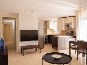Una habitación de hotel moderna con televisión de pantalla plana, una pequeña mesa de comedor, un banco y una zona de cocina con microondas.