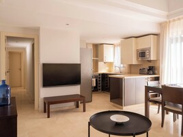 Una habitación de hotel moderna con televisión de pantalla plana, una pequeña mesa de comedor, un banco y una zona de cocina con microondas.