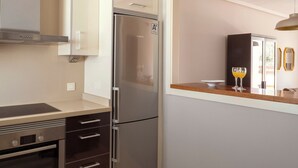 A compact kitchen with a stainless steel refrigerator, a built-in oven, and a microwave. There is a wooden countertop and a small dining area with two glasses of orange juice. - Ona Valle Romano Golf & Resort (Estepona)