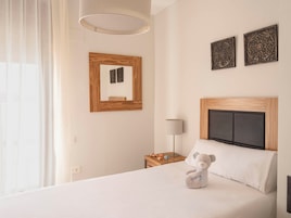 Habitación de hotel con cama, mesita de noche, lámpara, un peluche y dos adornos en la pared.