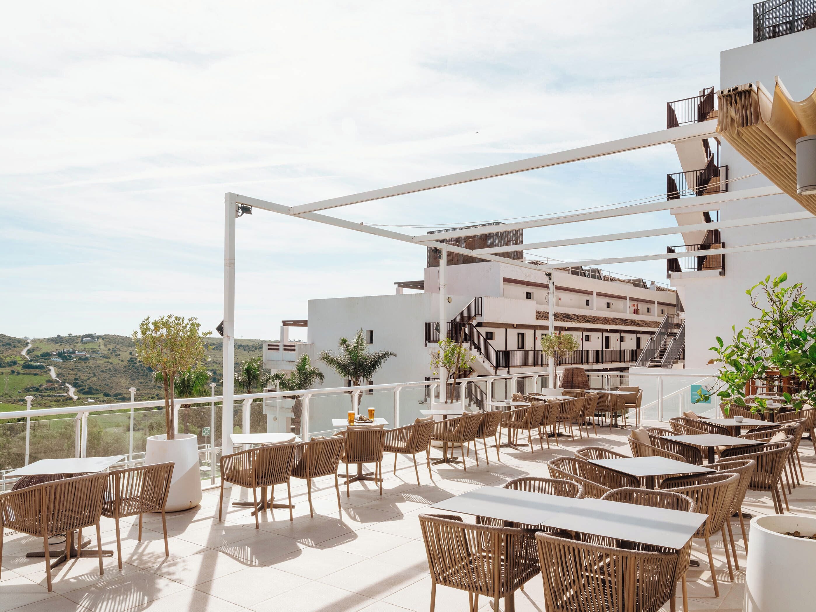 An outdoor terrace with tables and chairs, overlooking a hilly landscape.