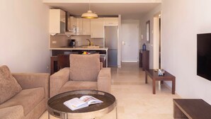 A modern living room with a sofa, a coffee table with a magazine, and a TV mounted on the wall. - Ona Valle Romano Golf & Resort (Estepona)