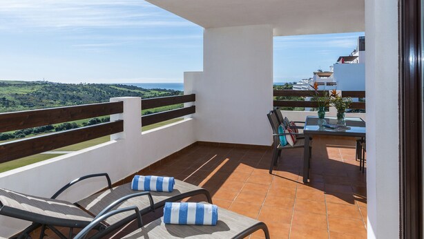 A balcony with a view of the countryside, a table with chairs, and a vase with flowers. - Ona Valle Romano Golf & Resort (Estepona)