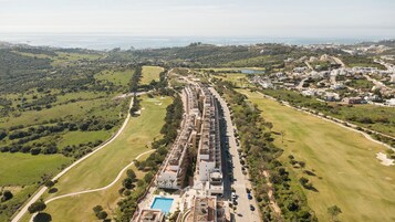 Vista aérea de una zona residencial con una larga calle bordeada de casas, una piscina y áreas verdes.