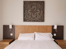 A hotel room with a wooden headboard, two bedside tables with lamps, and a decorative wall piece above the bed.