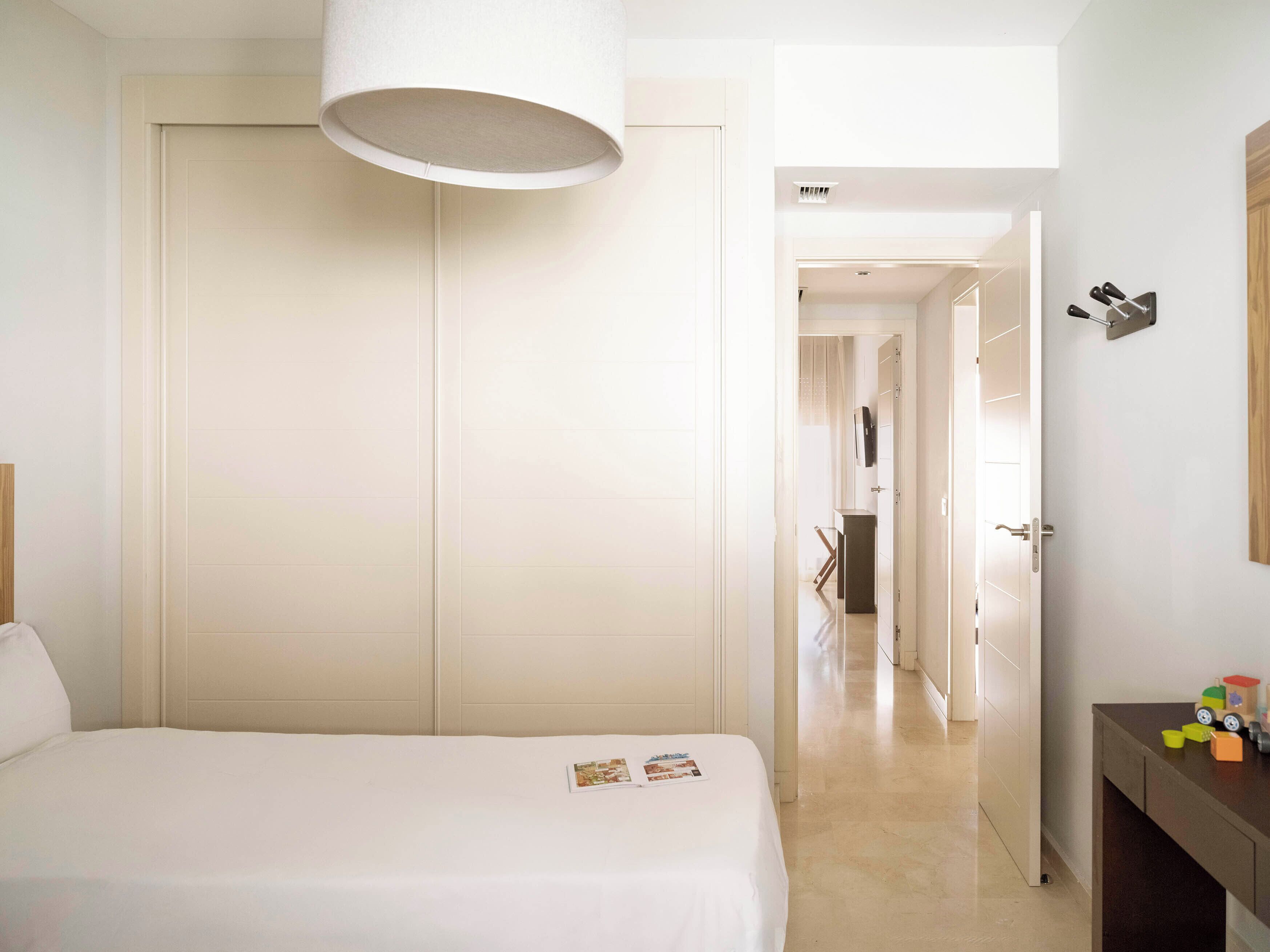 Una habitación de hotel con una cama, una mesita de noche, un armario y una puerta que da a otra estancia.