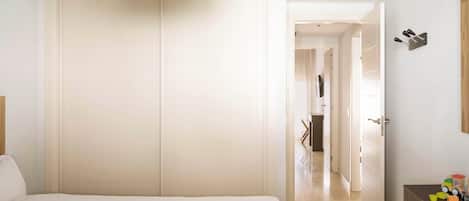 A hotel room with a bed, a bedside table, a wardrobe, and a door leading to another room.