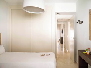 A hotel room with a bed, a bedside table, a wardrobe, and a door leading to another room. - Ona Valle Romano Golf & Resort (Estepona)