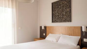 A hotel room with a bed, bedside lamps, a decorative wall piece, and a window with curtains.