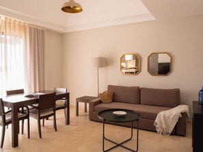 A living room with a sofa, a coffee table, a dining table with chairs, and a lamp. - Ona Valle Romano Golf & Resort (Estepona)
