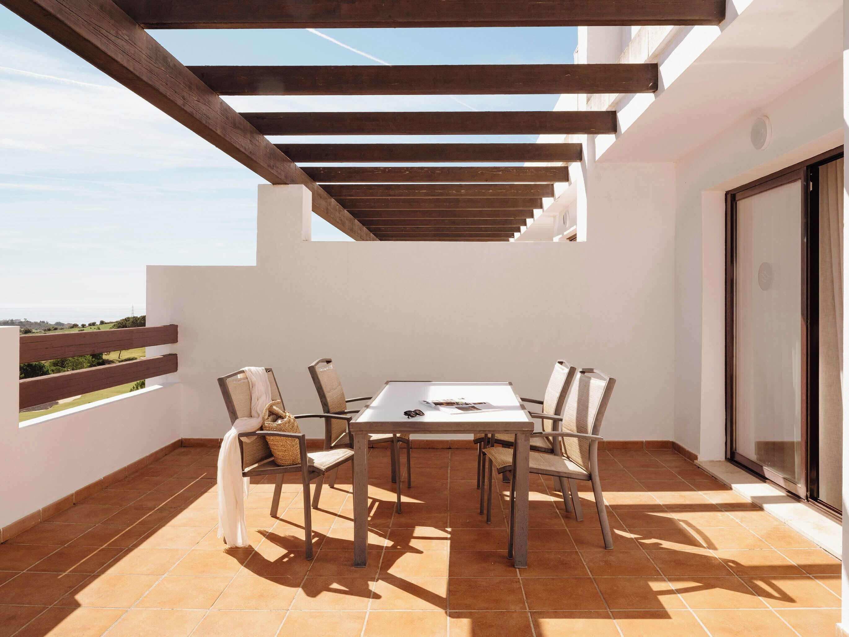 Eine Terrasse im Freien mit Tisch und Stühlen, einer Pergola darüber und Blick auf die Landschaft.