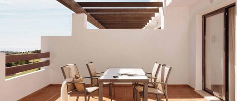 An outdoor patio with a table and chairs, a pergola overhead, and a view of the landscape.