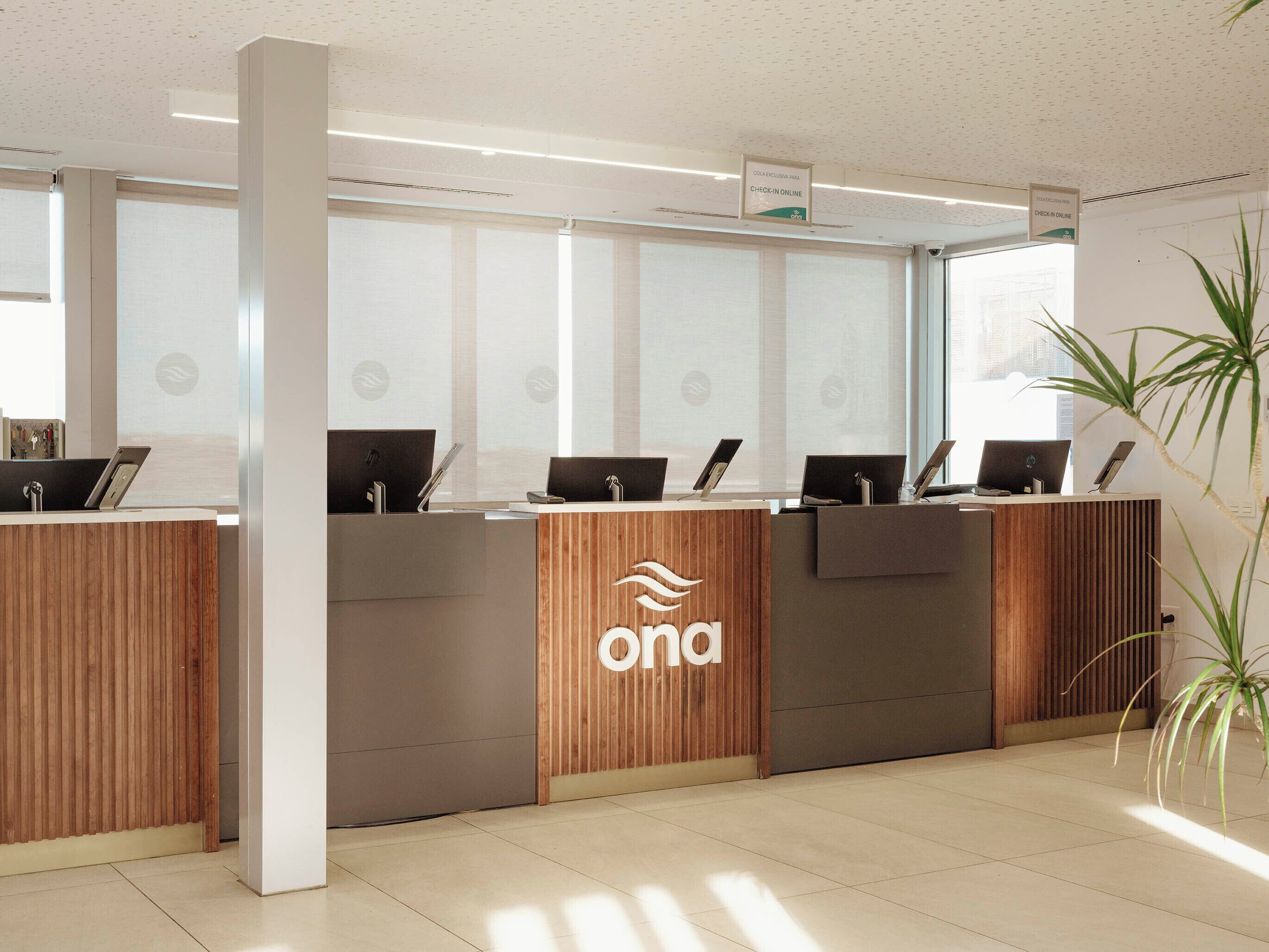 Un mostrador de recepción con varias estaciones de trabajo de ordenador, un logotipo en el centro y una planta en la esquina.