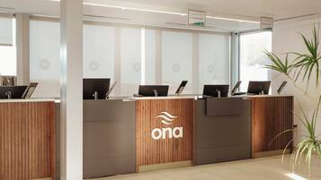 Un mostrador de recepción con varias estaciones de trabajo de ordenador, un logotipo en el centro y una planta en la esquina.