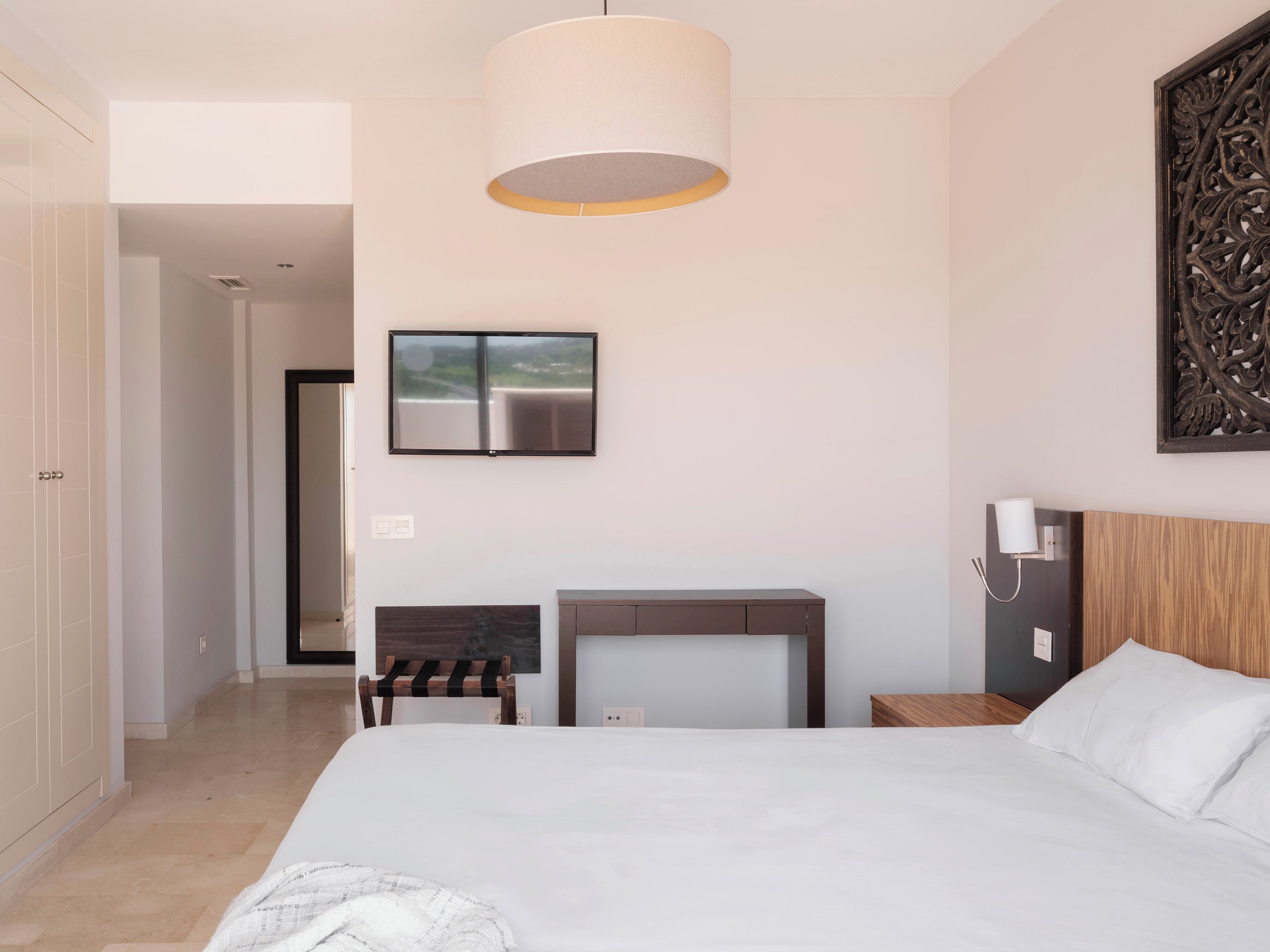 Una habitación de hotel moderna con una cama grande, un televisor de pantalla plana, un cabecero de madera, una mesita de noche y un adorno en la pared.