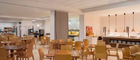 Una amplia cafetería con mesas y sillas de madera, una zona de bufé y una pantalla de televisión.