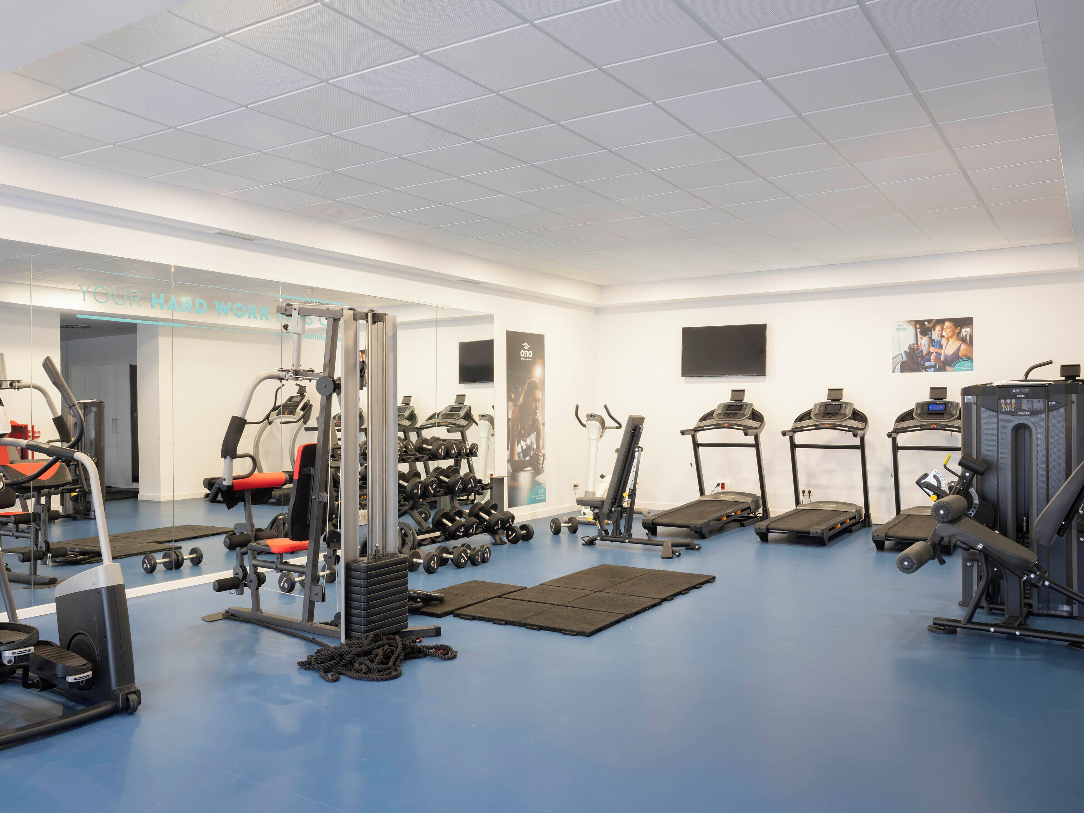 Un gimnasio con varios equipos de ejercicio, incluyendo cintas de correr, mancuernas y máquinas de pesas.