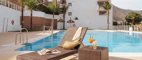 A poolside area with lounge chairs, a small table with a drink, and a lifebuoy on the wall.