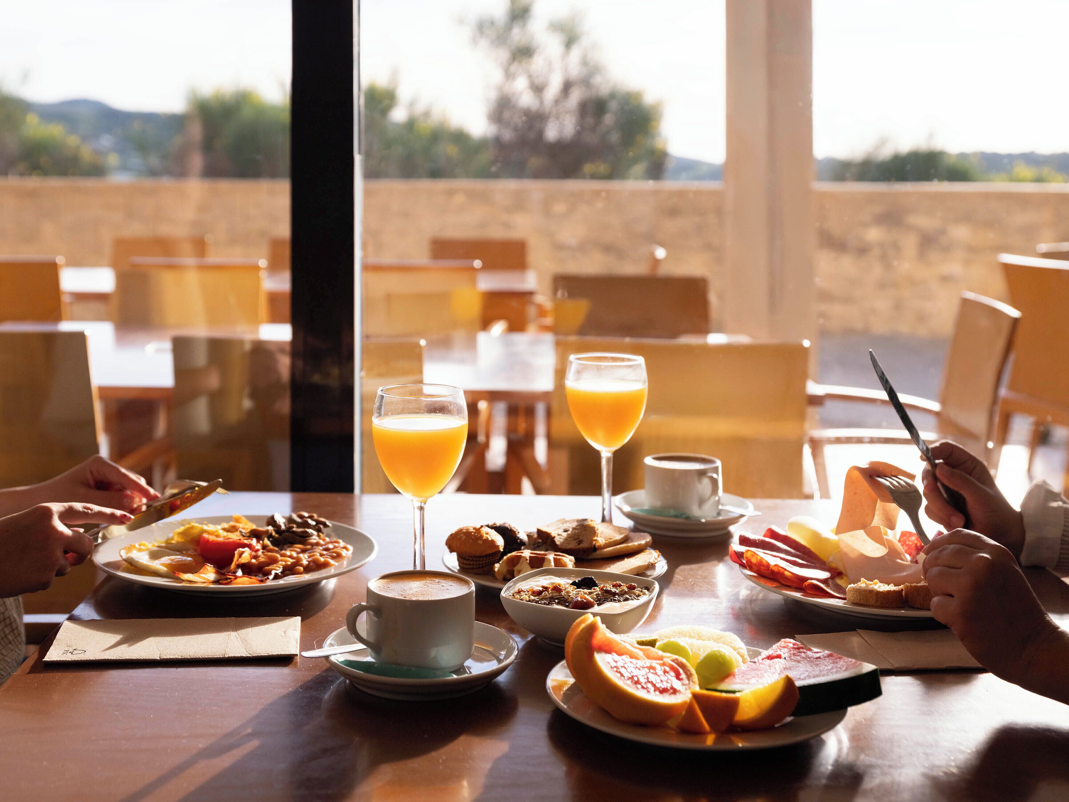 Ein Esstisch mit Frühstücksgebäck, ein Glas Orangensaft und eine Tasse Kaffee, vor einer schönen Aussicht.