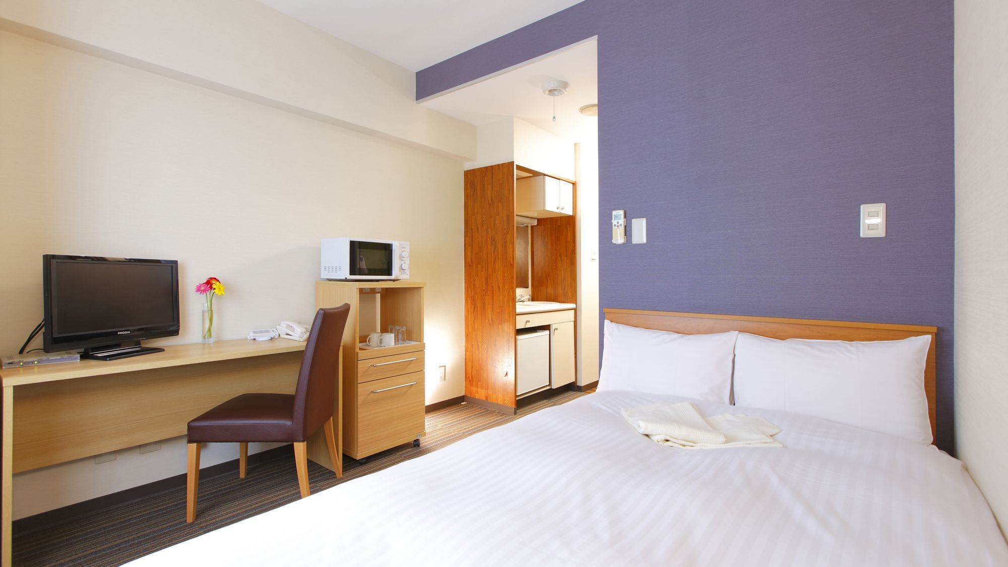 Habitación de hotel con cama, escritorio con televisor, una silla, microondas, espejo y baño.