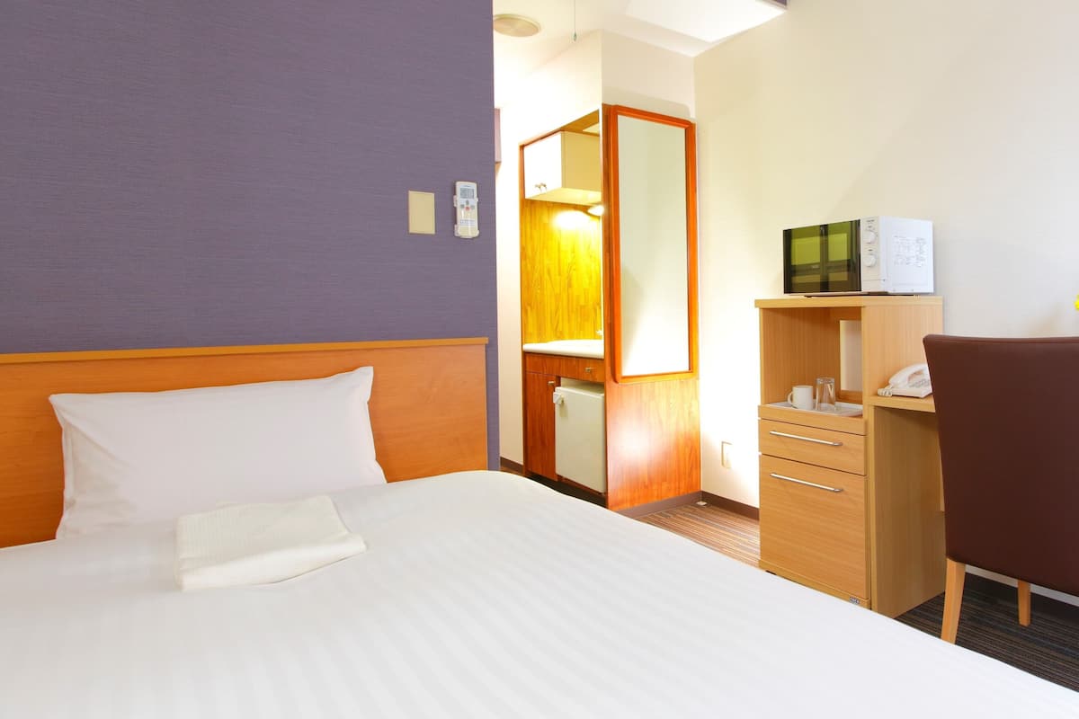 A hotel room with a bed, a desk, a chair, a wardrobe, and a mirror.