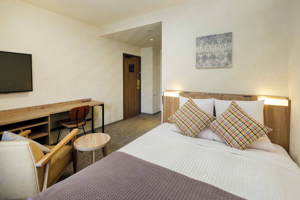 Una habitación de hotel con cama, escritorio, silla, televisor y puerta.