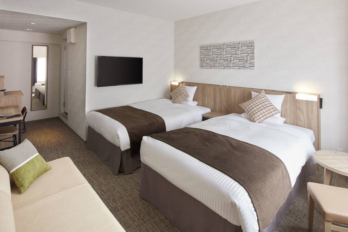 Una habitación de hotel con dos camas, un televisor, un espejo, un escritorio y una silla.