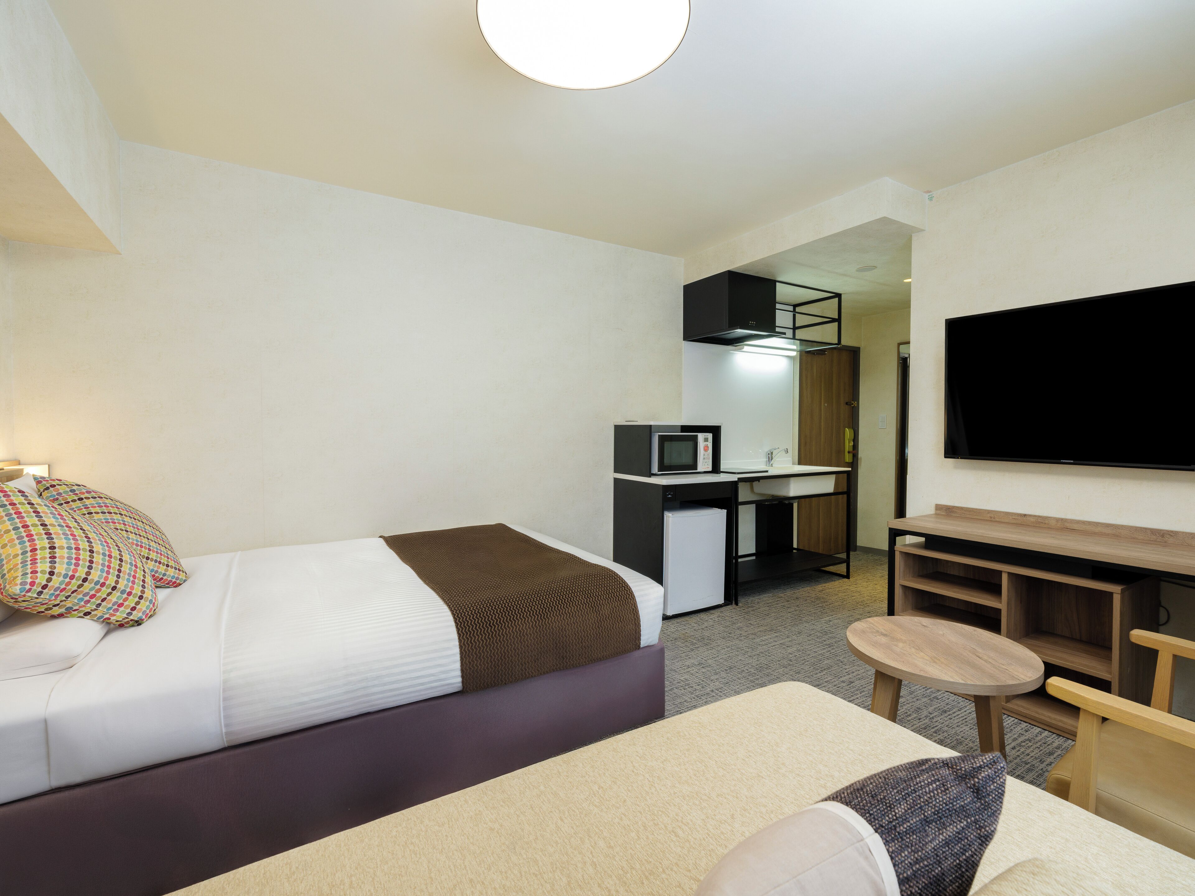 A modern hotel room with a bed, a desk with a computer, a TV, and a small seating area.