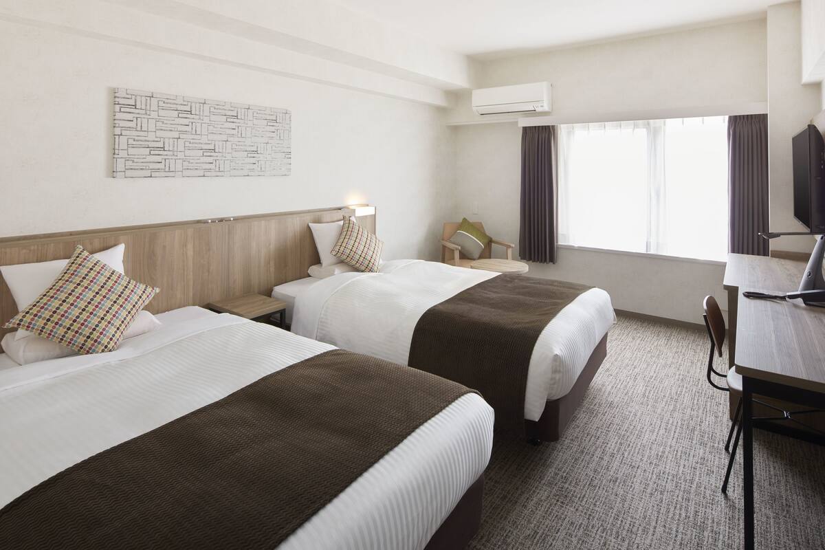 Una habitación de hotel con dos camas, un escritorio, una silla, un televisor y un equipo de aire acondicionado.