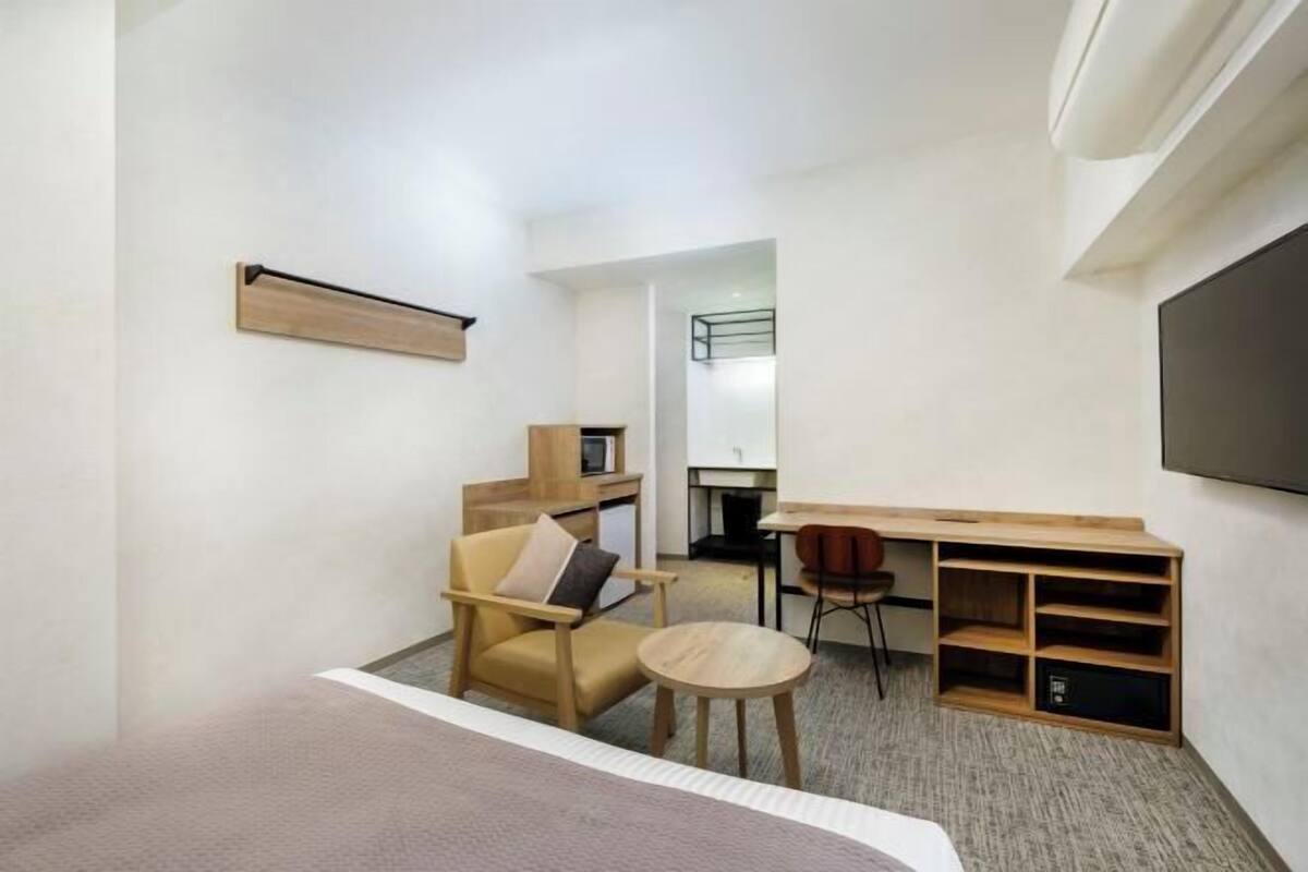 Habitación de hotel pequeña con cama, escritorio, silla, mesita y televisor.