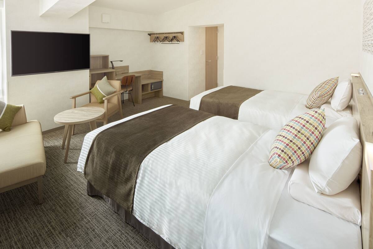 Una habitación de hotel con dos camas, un escritorio, una silla y un televisor.