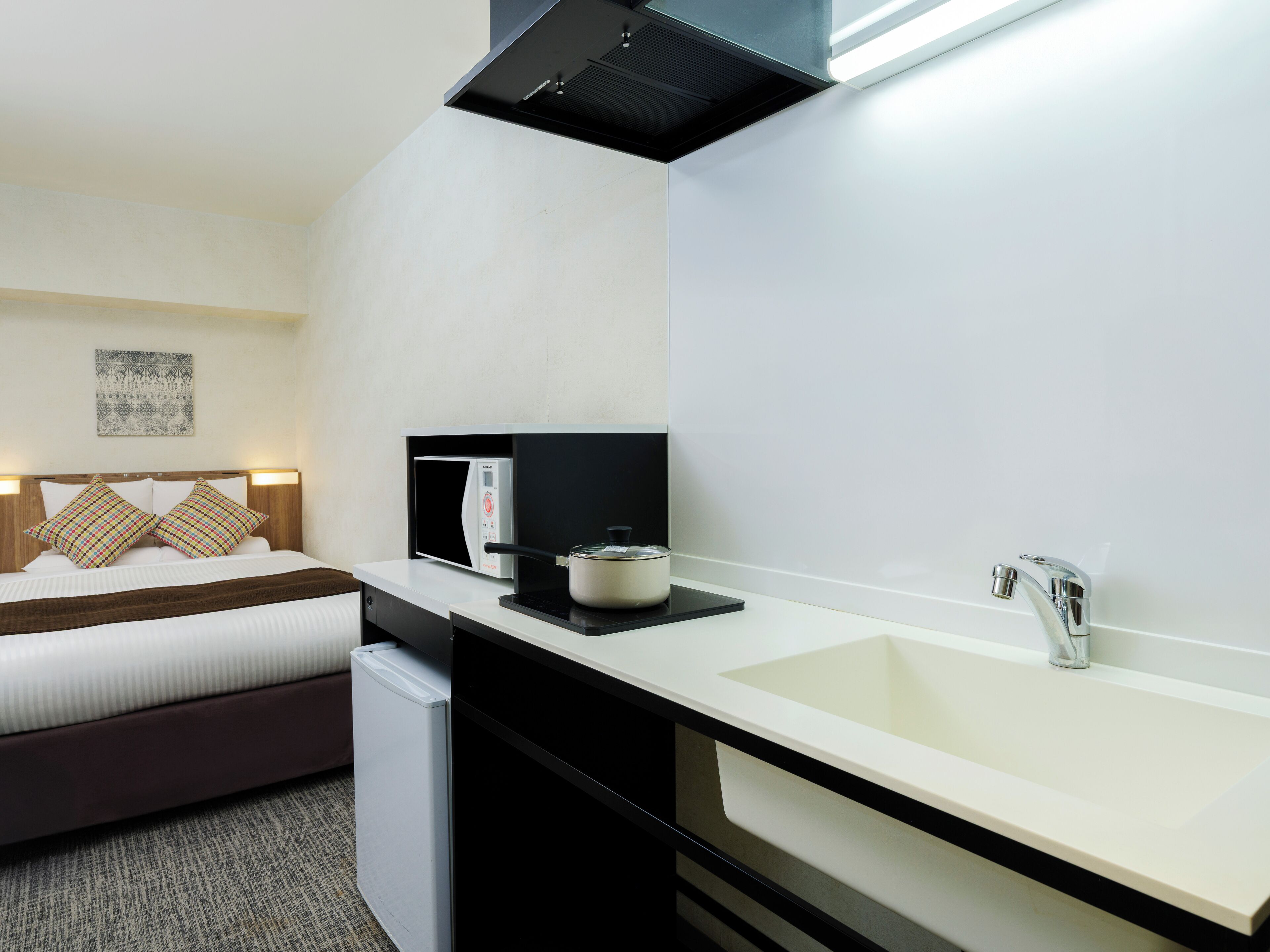 Een kleine hotelkamer met een bed, een kitchenette en een badkamer.