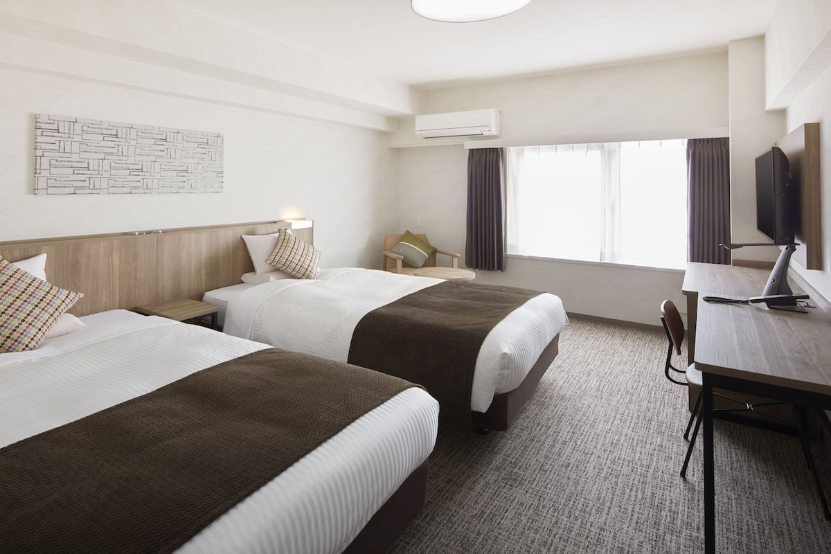 Habitación de hotel con dos camas, un escritorio con silla, televisión y aire acondicionado.