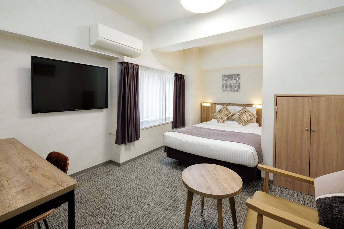 Una habitación de hotel con cama, televisor, escritorio, silla y armario.