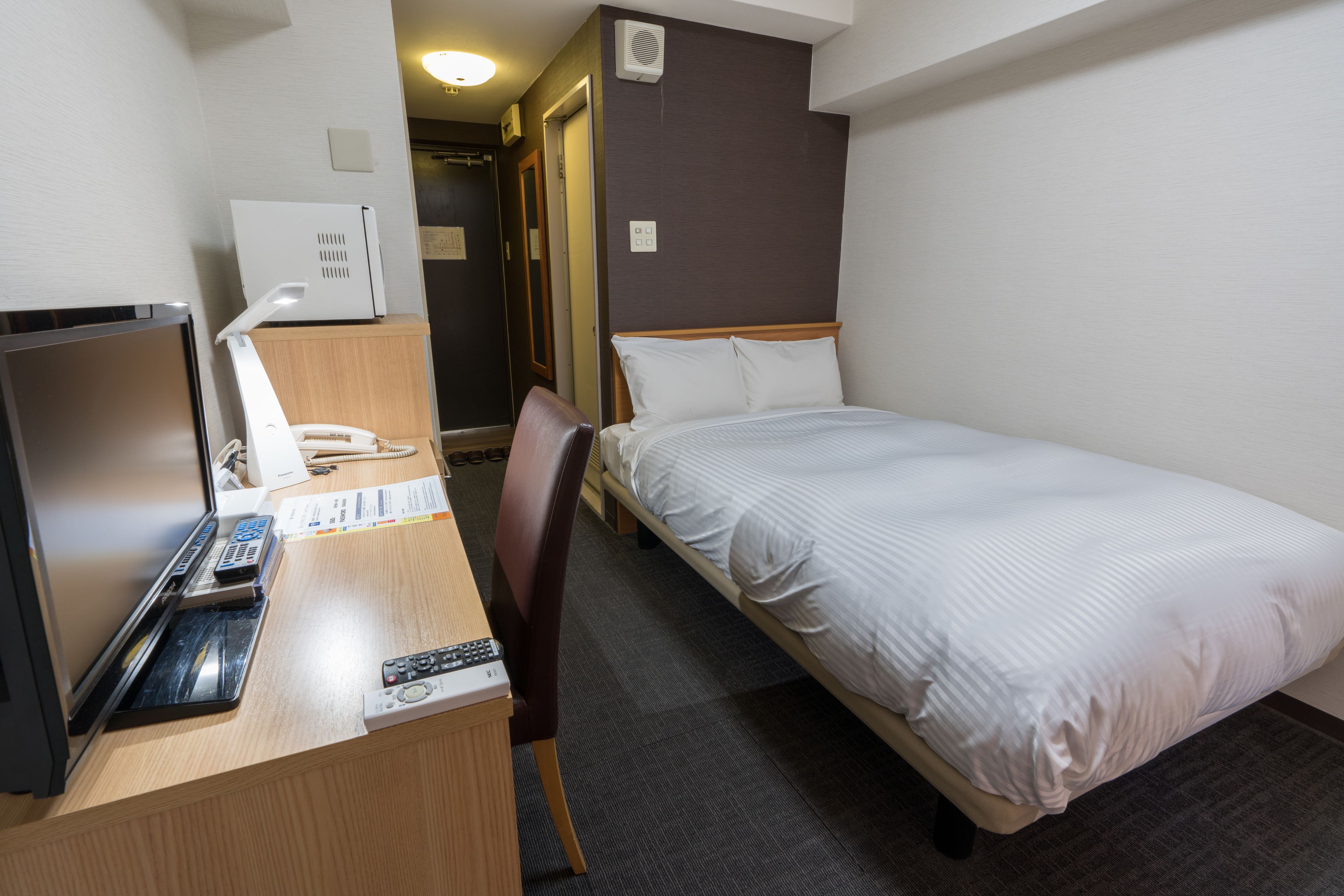 A hotel room with a bed, a desk with a computer, a chair, and a television.