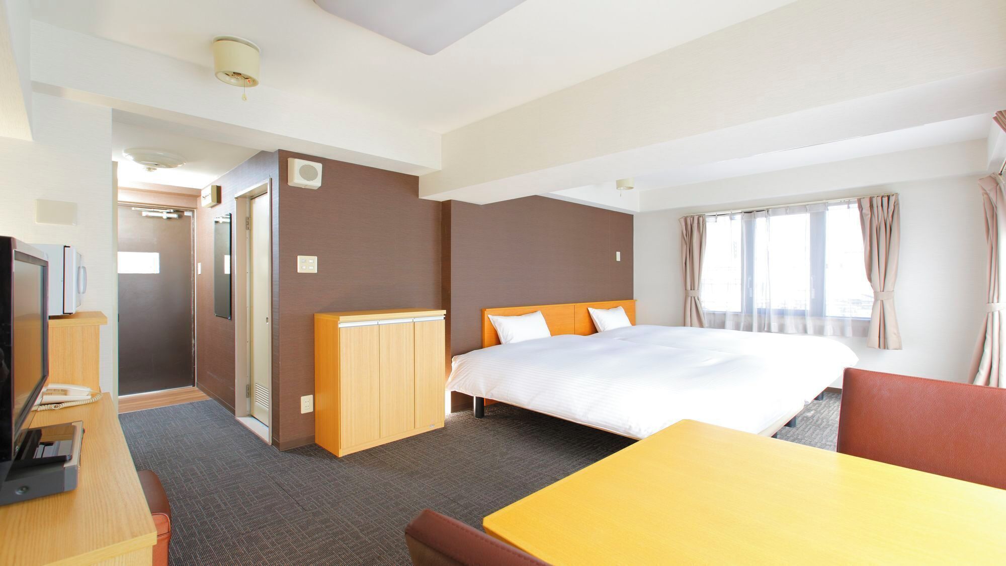A hotel room with a bed, a desk, a chair, a wardrobe, and a shower.