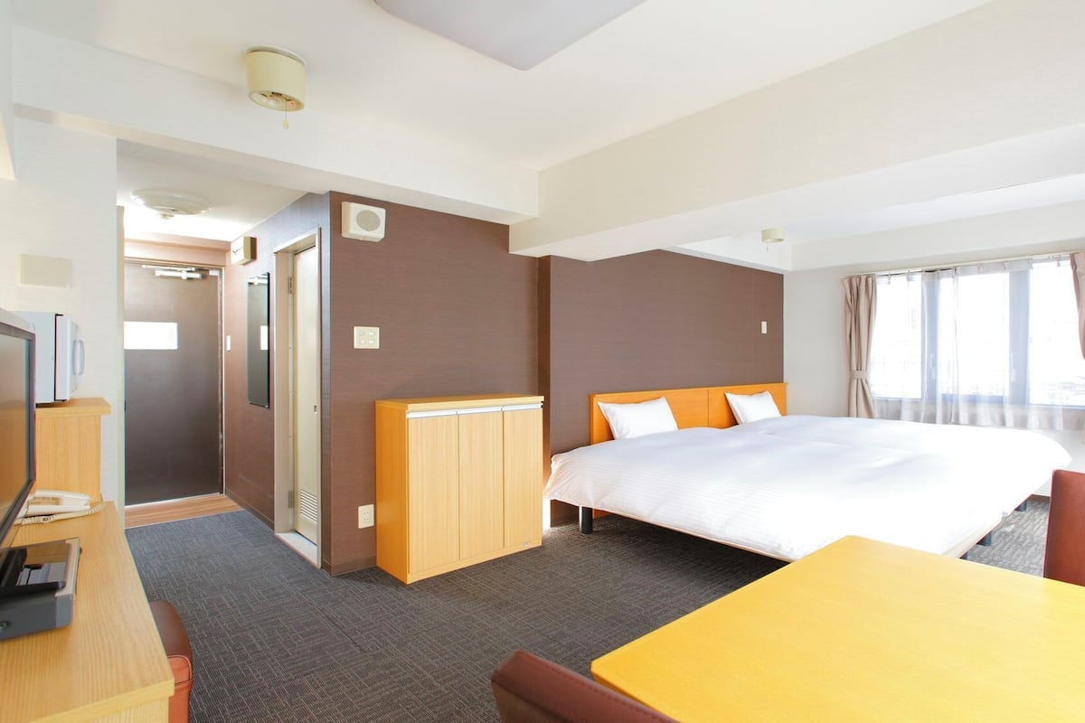 A hotel room with a bed, a desk, a chair, a wardrobe, and a shower.
