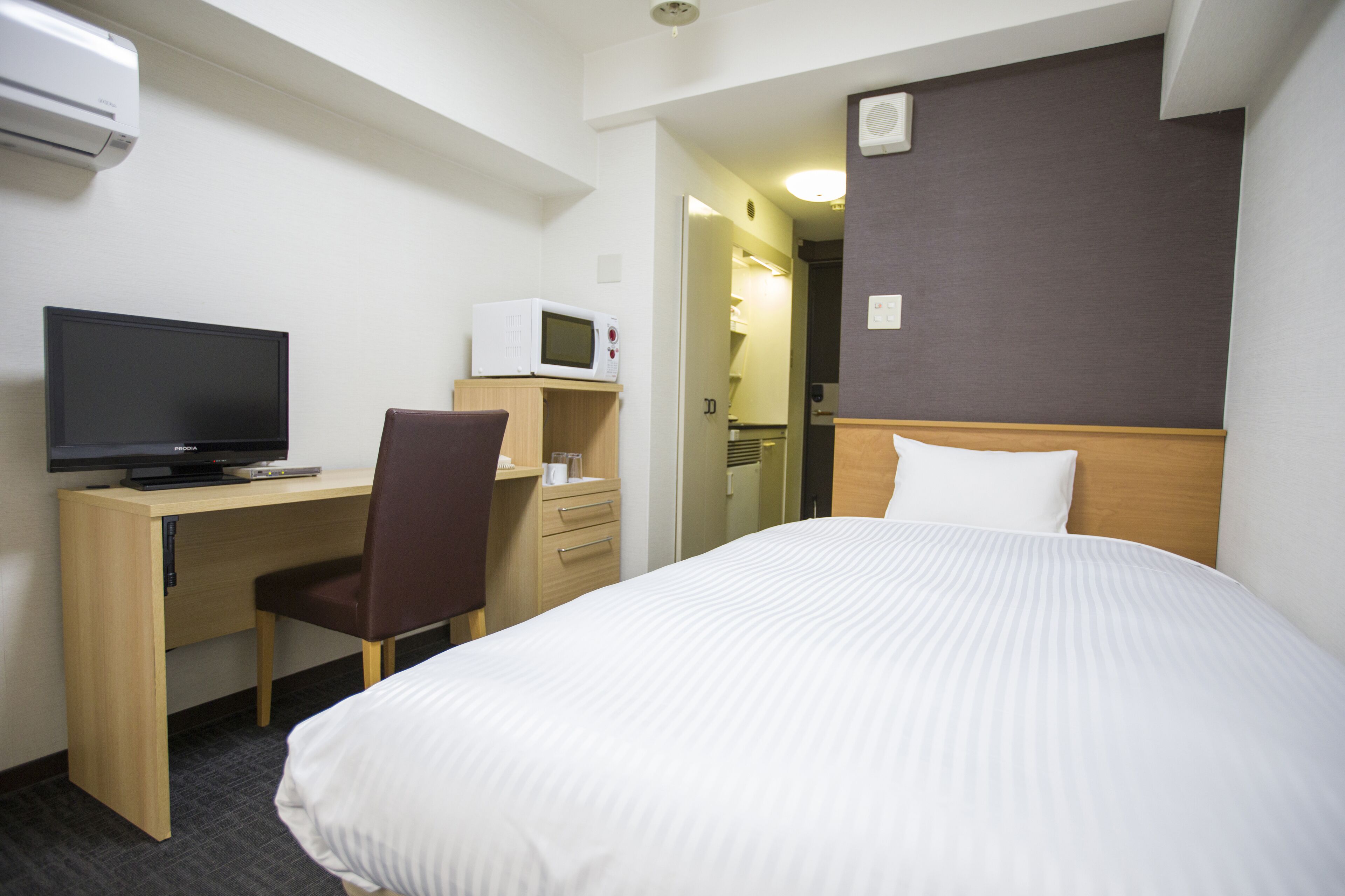 A hotel room with a bed, a desk with a computer and a microwave, and a chair.