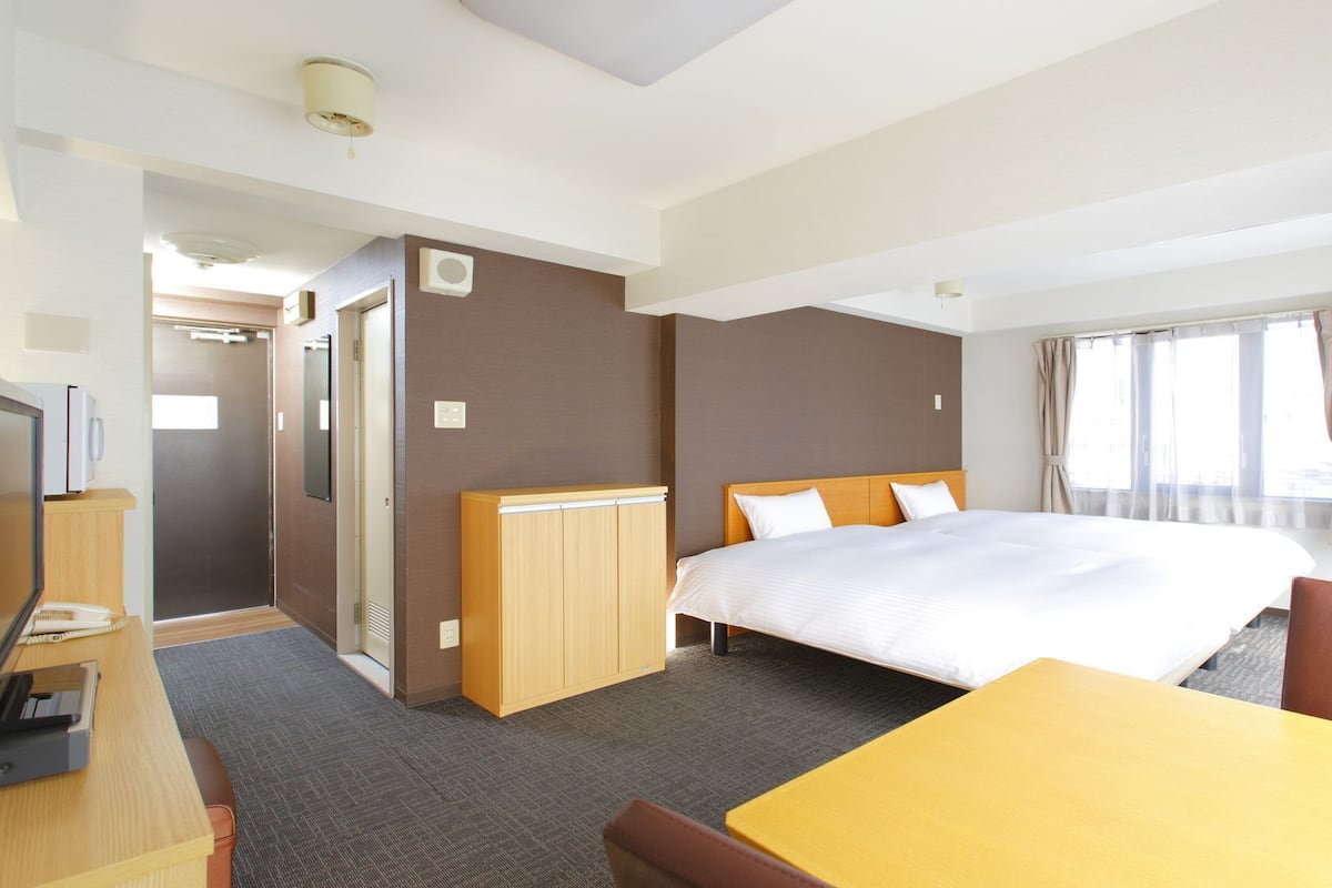 A hotel room with a bed, a desk, a chair, a wardrobe, and a shower.