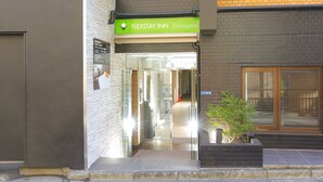 The entrance to FLEXSTAY INN Shirogane with a clear glass door, a small potted plant, and a sign above the door. - Flexstay Inn Shirogane (Tokyo)